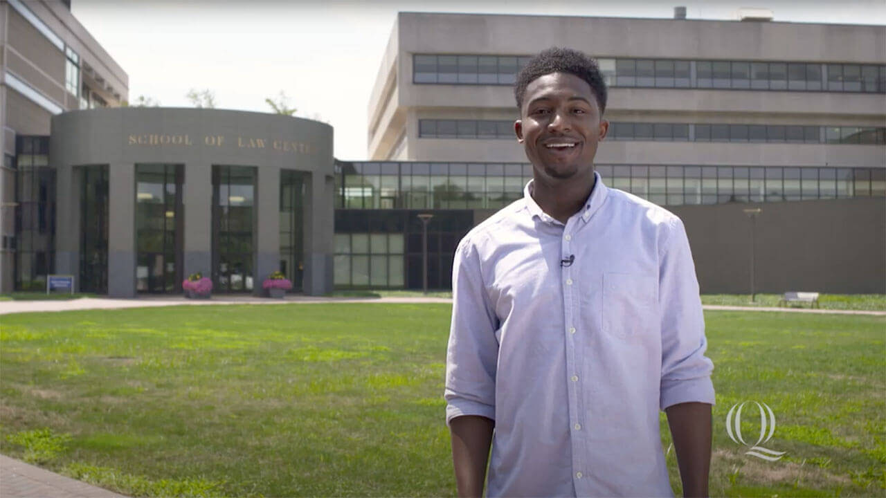 A law student stands outside the main entrance of the School of Law Center, starts video