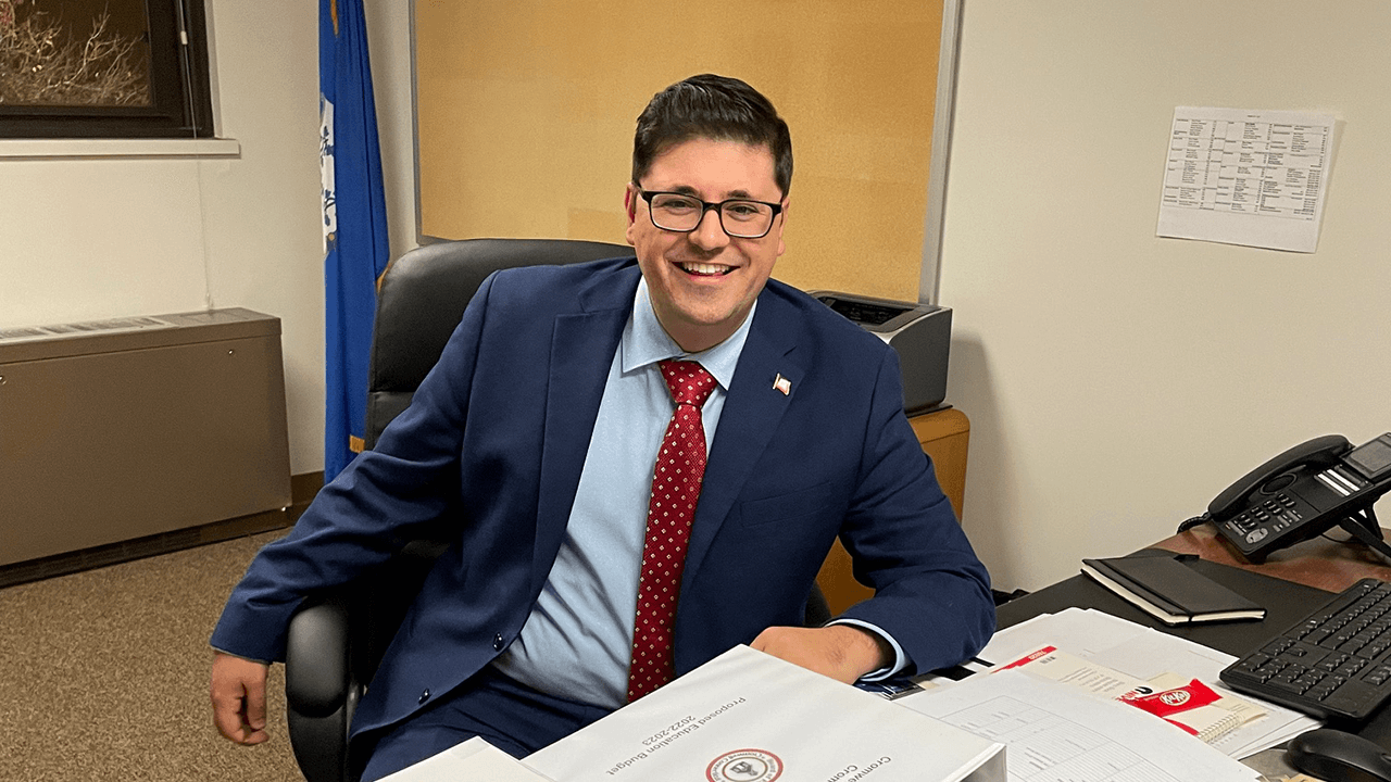 James Demetriades sitting at a desk in a blue suit.